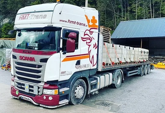Weißer HMT-Scania mit Plateausattel, Ladung mit orangen Gurten gesichert