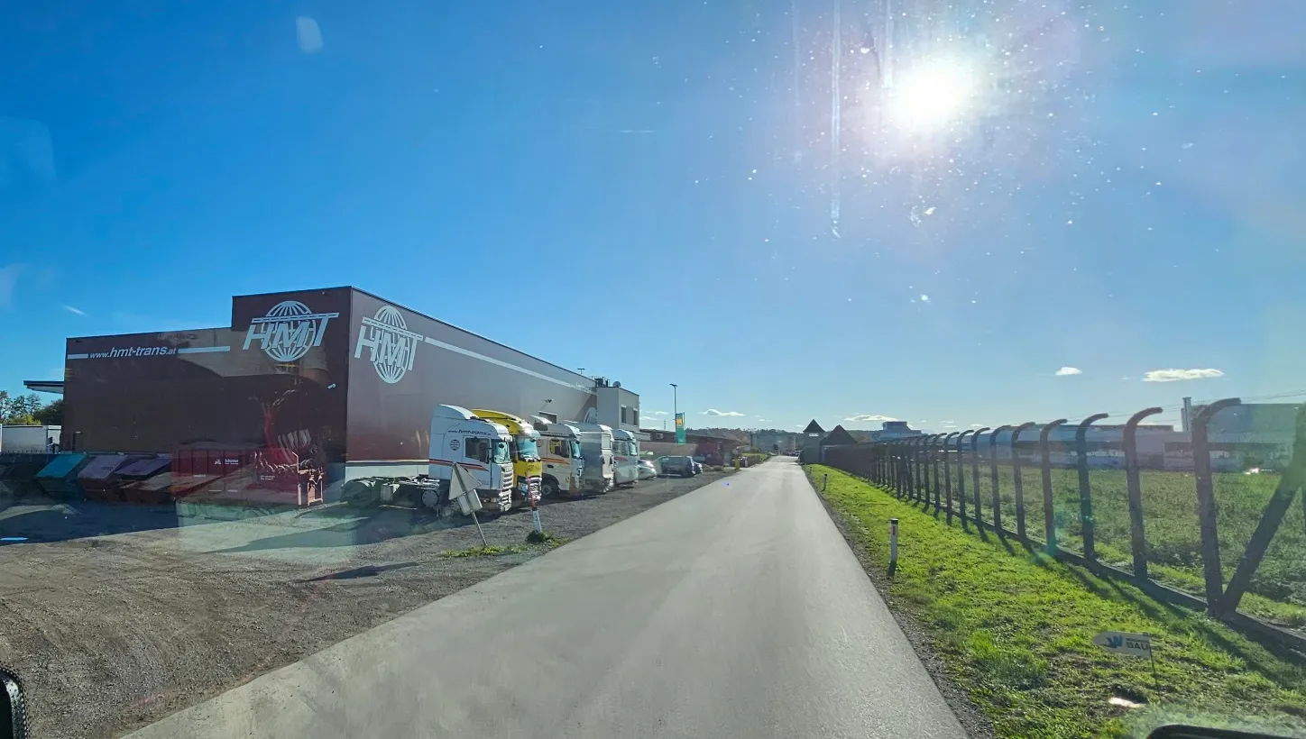 Rote HMT-Halle mit Logo und Lkw an der Zufahrtsstraße in Asten