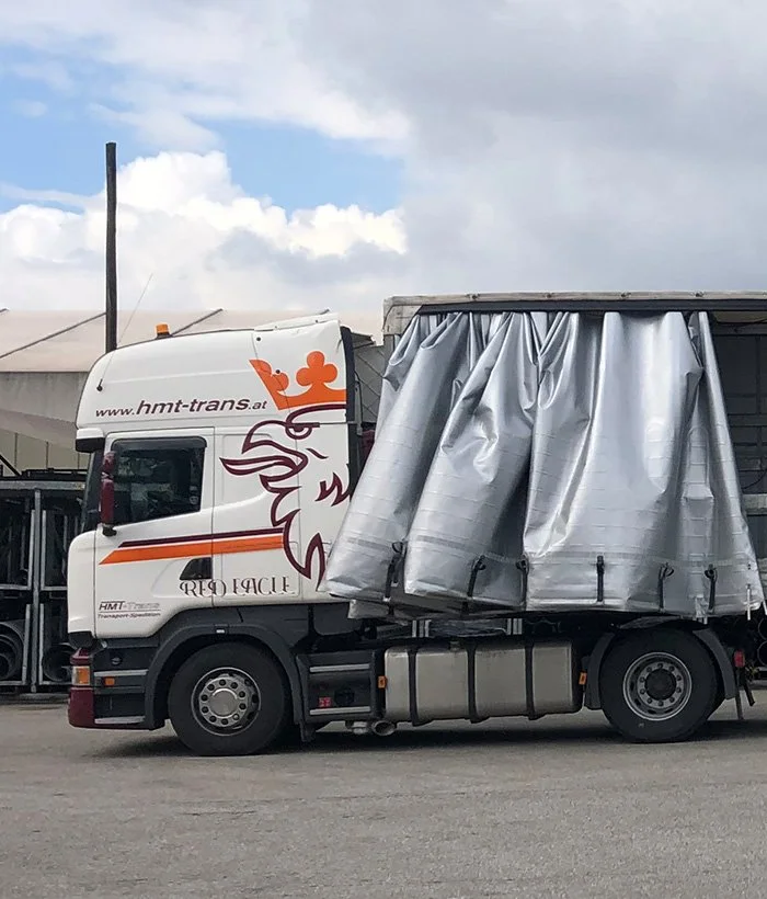Weißer HMT-Scania mit der Aufschrift www.hmt-trans.at und geöffnetem Planensattel